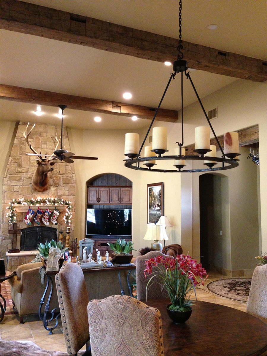 A living room filled with decorations including a deer head and a chandelier hanging from reclaimed hand-hewn timber beams